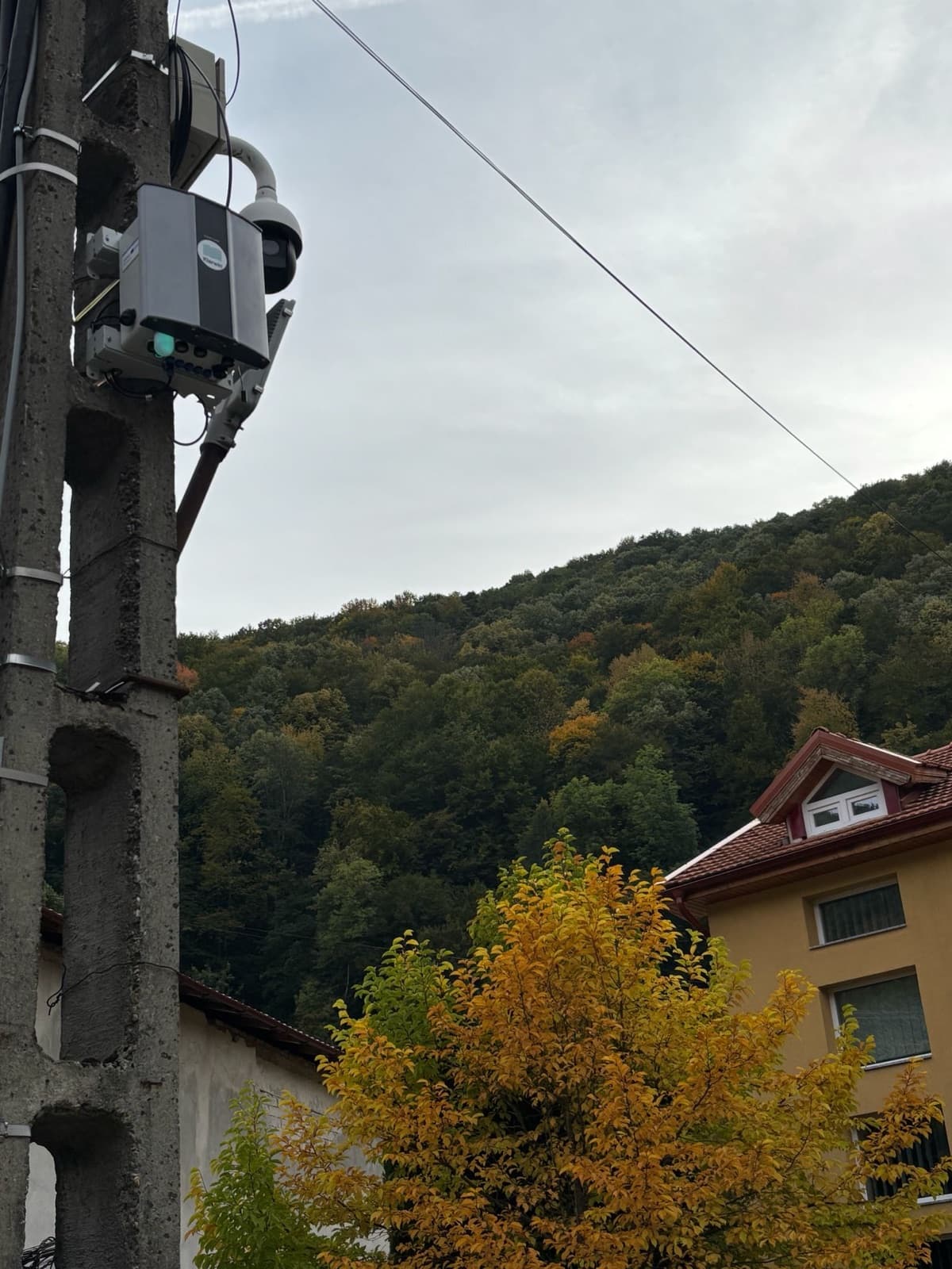 An Oizom Polludrone station mounted high on a concrete utility pole, with a wooded hillside behind, in Timiș County